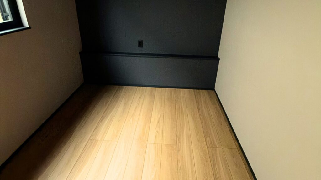 １階：木目の床に濃いアクセント壁を組み合わせた落ち着きのある空間。ベッドまわりで使えるカウンターとコンセントも設けています。